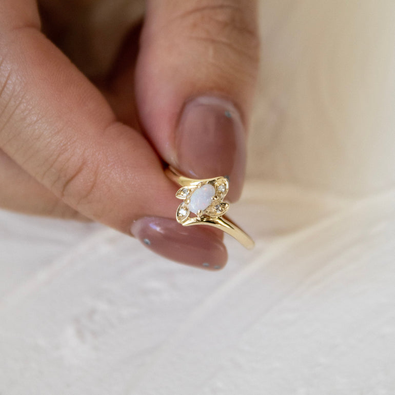 Gold ring with a central gemstone held between fingers on a light background
