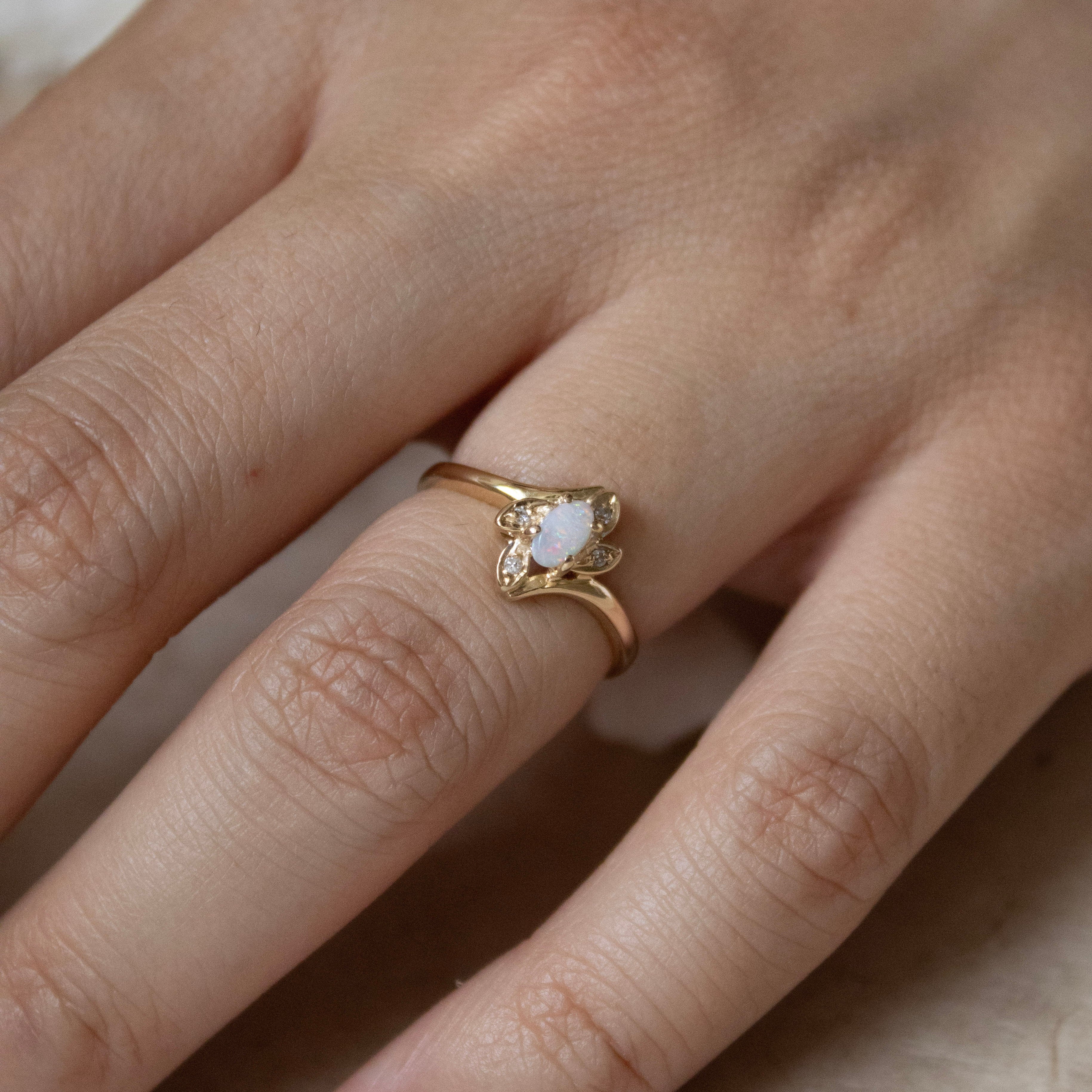 Hand wearing a gold ring with a white stone on a neutral background