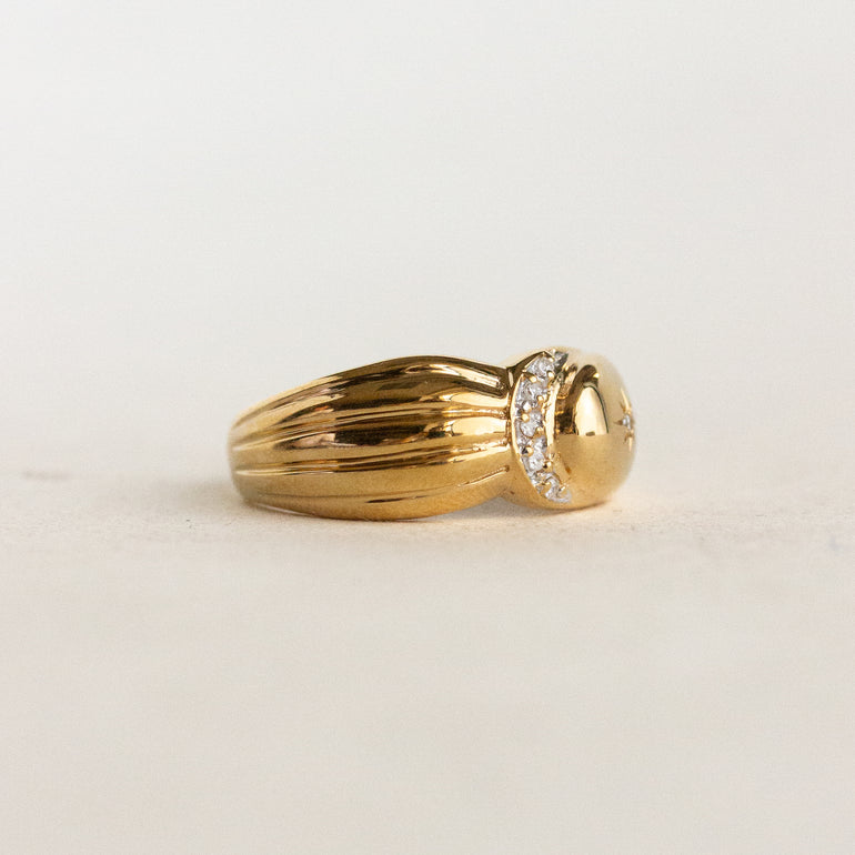 Gold ring with a diamond-studded design on a light beige background