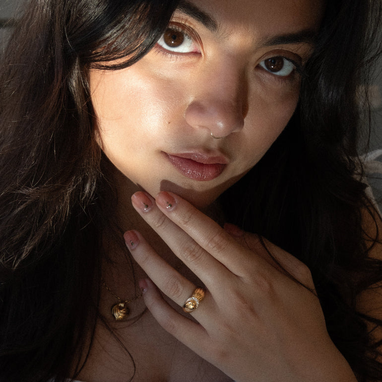 Close-up of a person with a hand near their face, wearing gold jewelry.