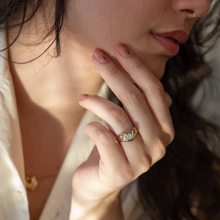 Close-up of a person wearing a gold ring and necklace, with a soft focus on the background.