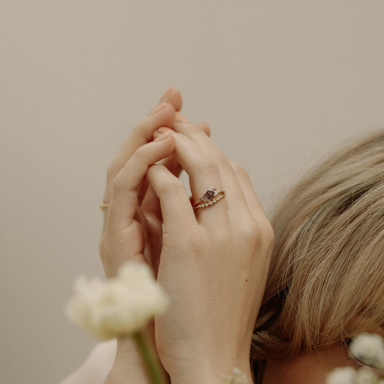 Close-up of hands with a ring, surrounded by flowers against a neutral background