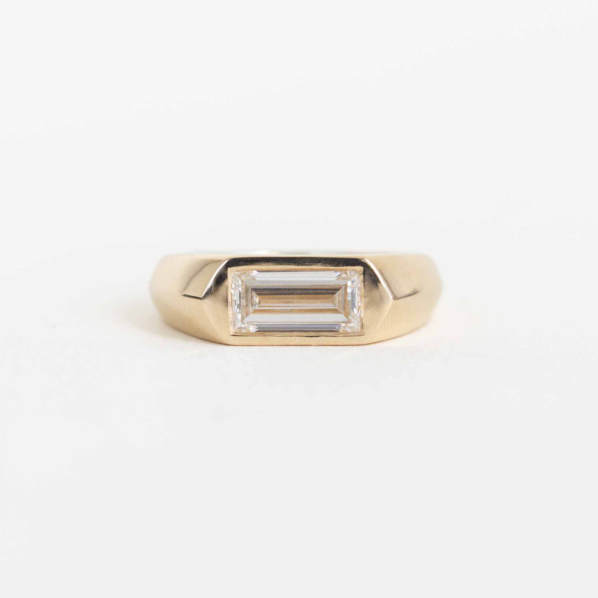 A gold ring with a rectangular baguette-cut clear gemstone, shown on a plain white background