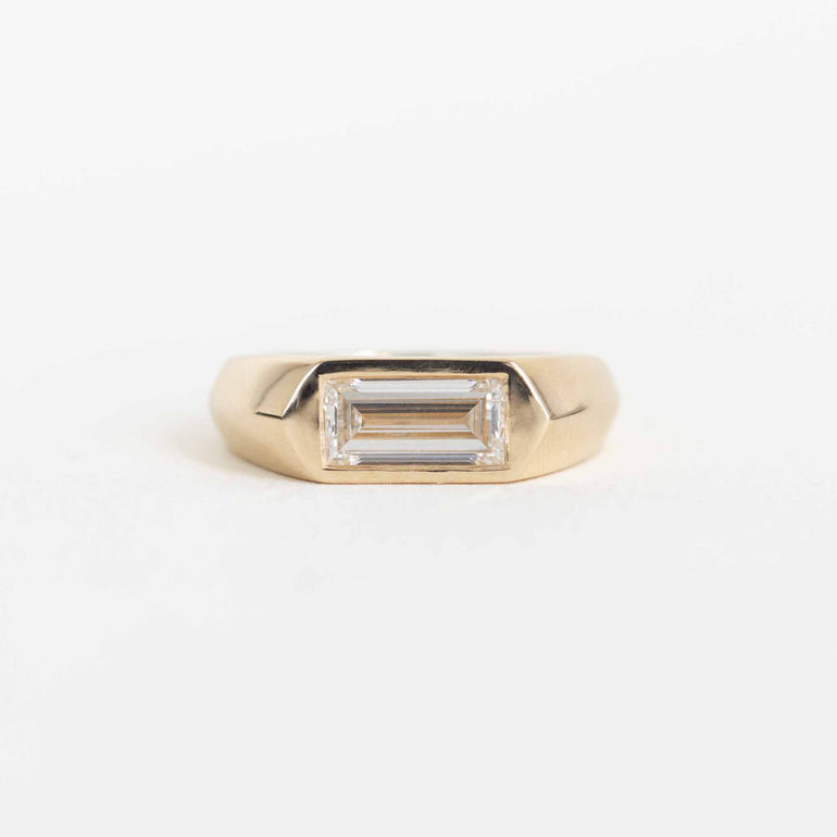 A gold ring with a rectangular baguette-cut clear gemstone, shown on a plain white background