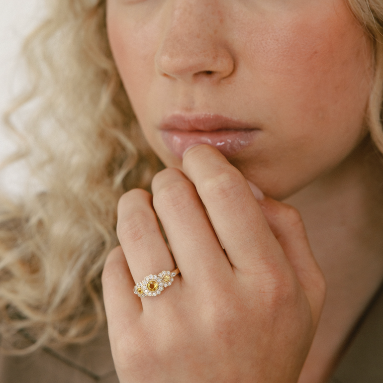 Woman with curly blonde hair wearing a gold ring on her finger, looking to the side.
