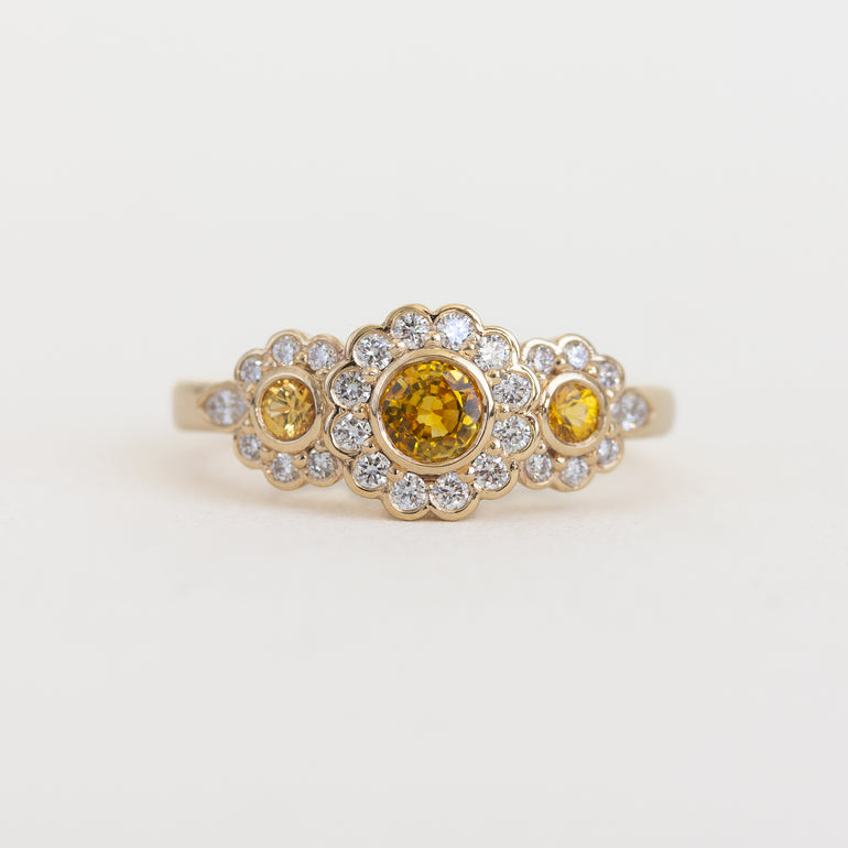 Gold ring with yellow gemstones and diamond accents on a light background