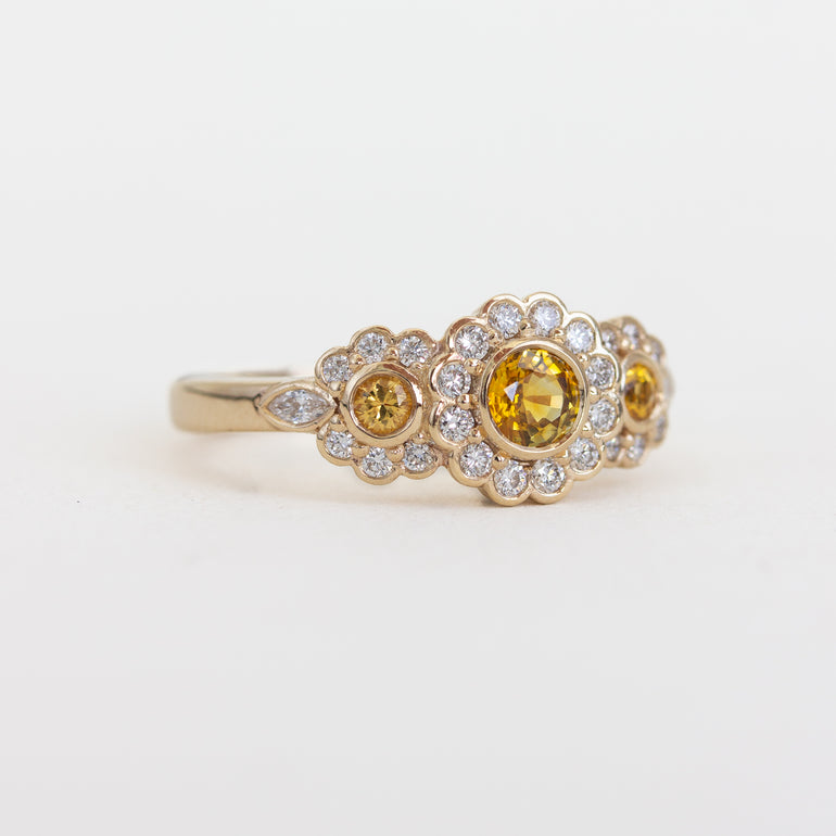 Gold ring with yellow gemstones and diamond accents on a white background