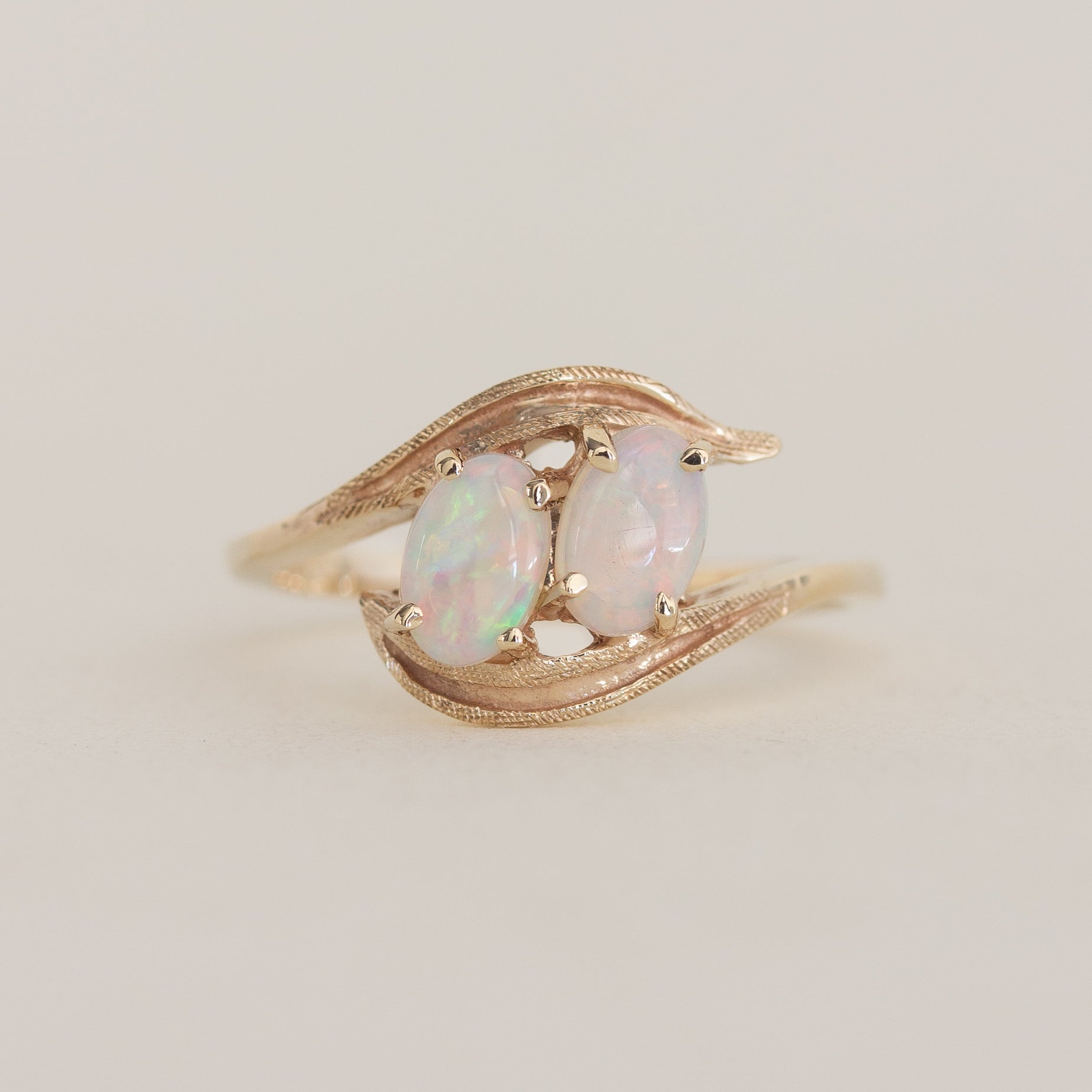 Gold ring with two opal stones on a light beige background