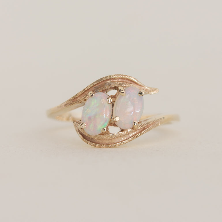 Gold ring with two opal stones on a light beige background