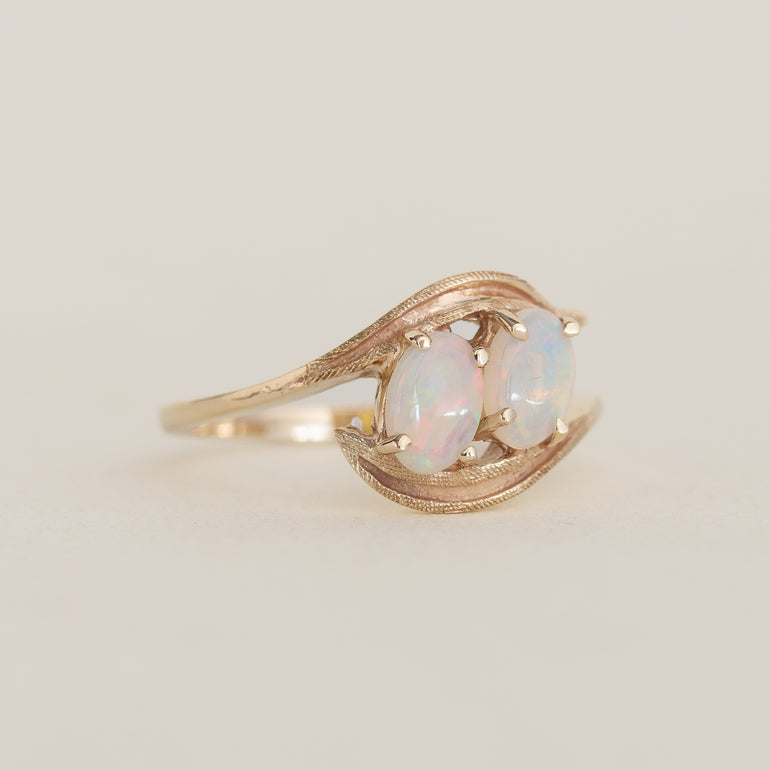 Gold ring with two opal stones on a light beige background