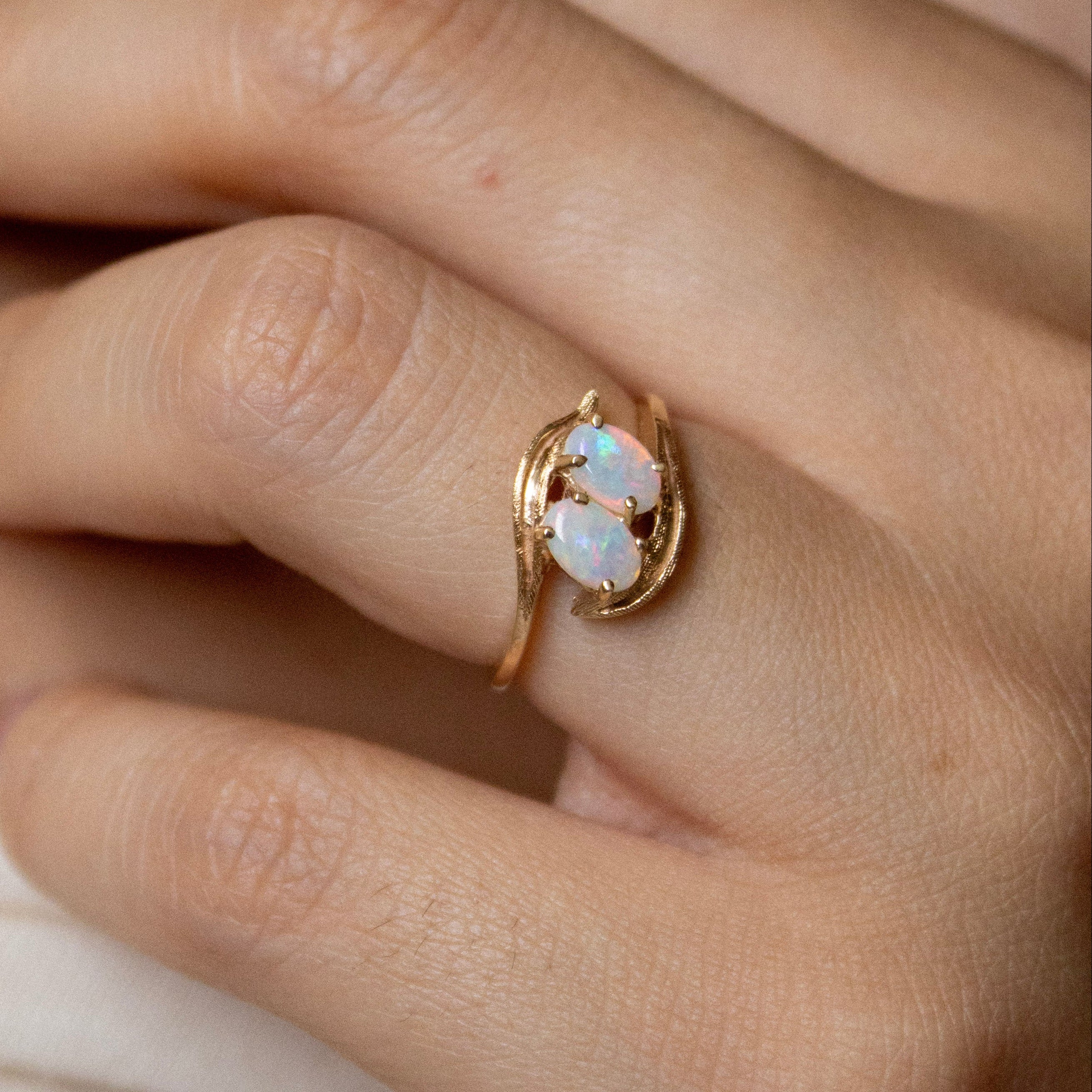 Close-up of a hand wearing a gold ring with a stone, against a neutral background.
