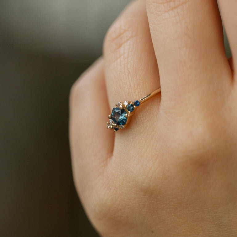 Close-up of a hand wearing a ring with blue gemstones on a blurred background