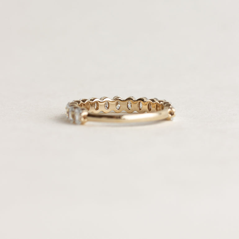 A yellow gold eternity ring with a continuous row of small round-cut clear gemstones, photographed on a plain off-white background.