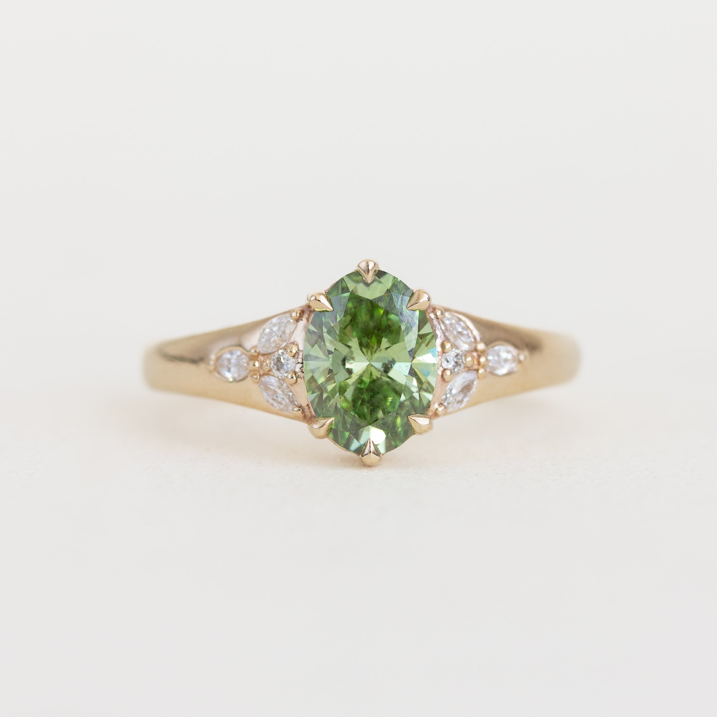 Gold ring with a green gemstone and small diamonds on a light background