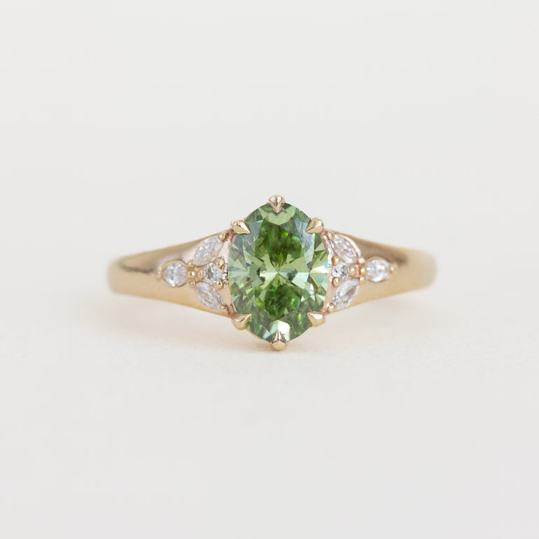 Gold ring with a green gemstone and small diamonds on a light background