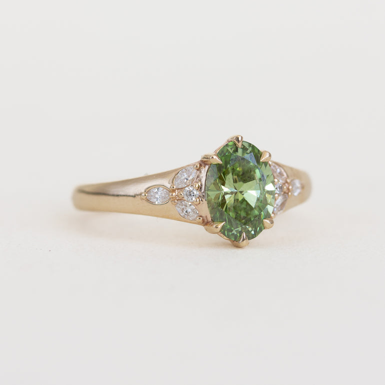 Gold ring with a green gemstone and small diamonds on a light background