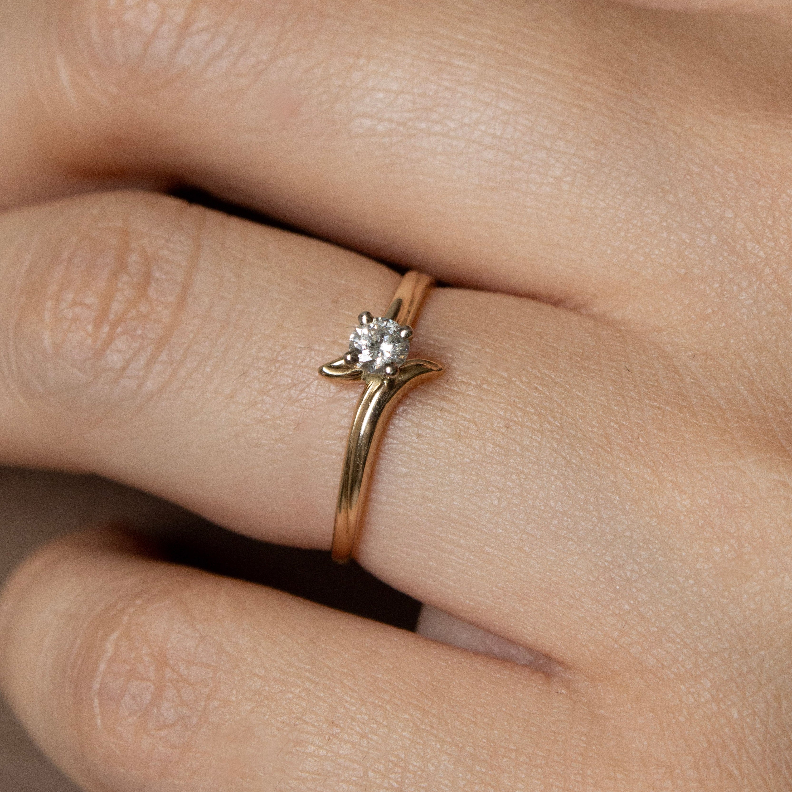 Close-up of a hand wearing a gold ring with a diamond on a neutral background