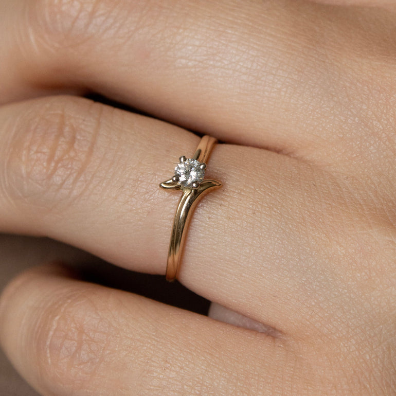 Close-up of a hand wearing a gold ring with a diamond on a neutral background
