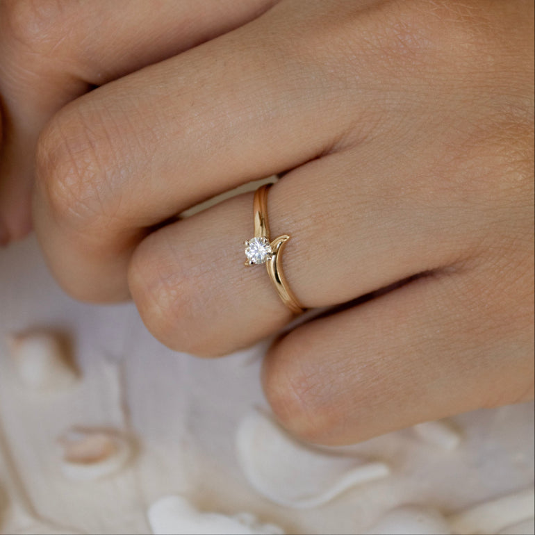 Hand wearing a gold ring with a diamond on a background of seashells