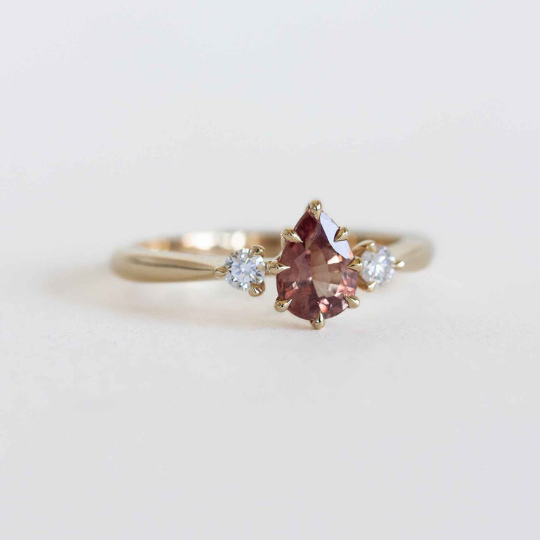 Gold ring with a berry sapphire and two smaller diamonds on a light gray background.