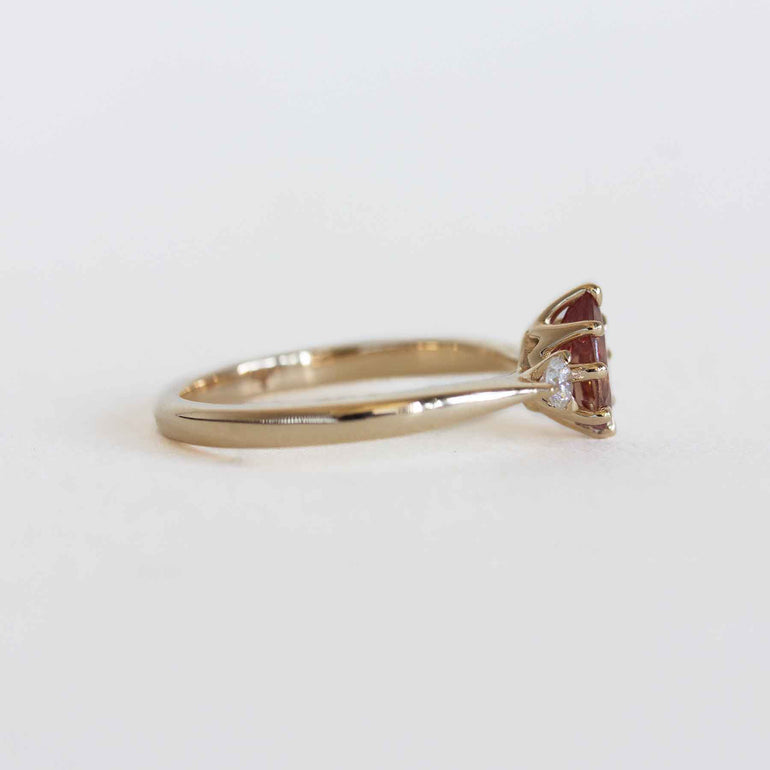 Gold ring with a berry sapphire and two smaller diamonds on a light gray background.