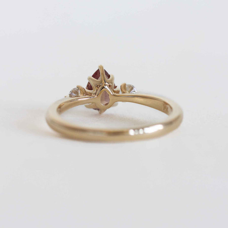 Gold ring with a berry sapphire and two smaller diamonds on a light gray background.