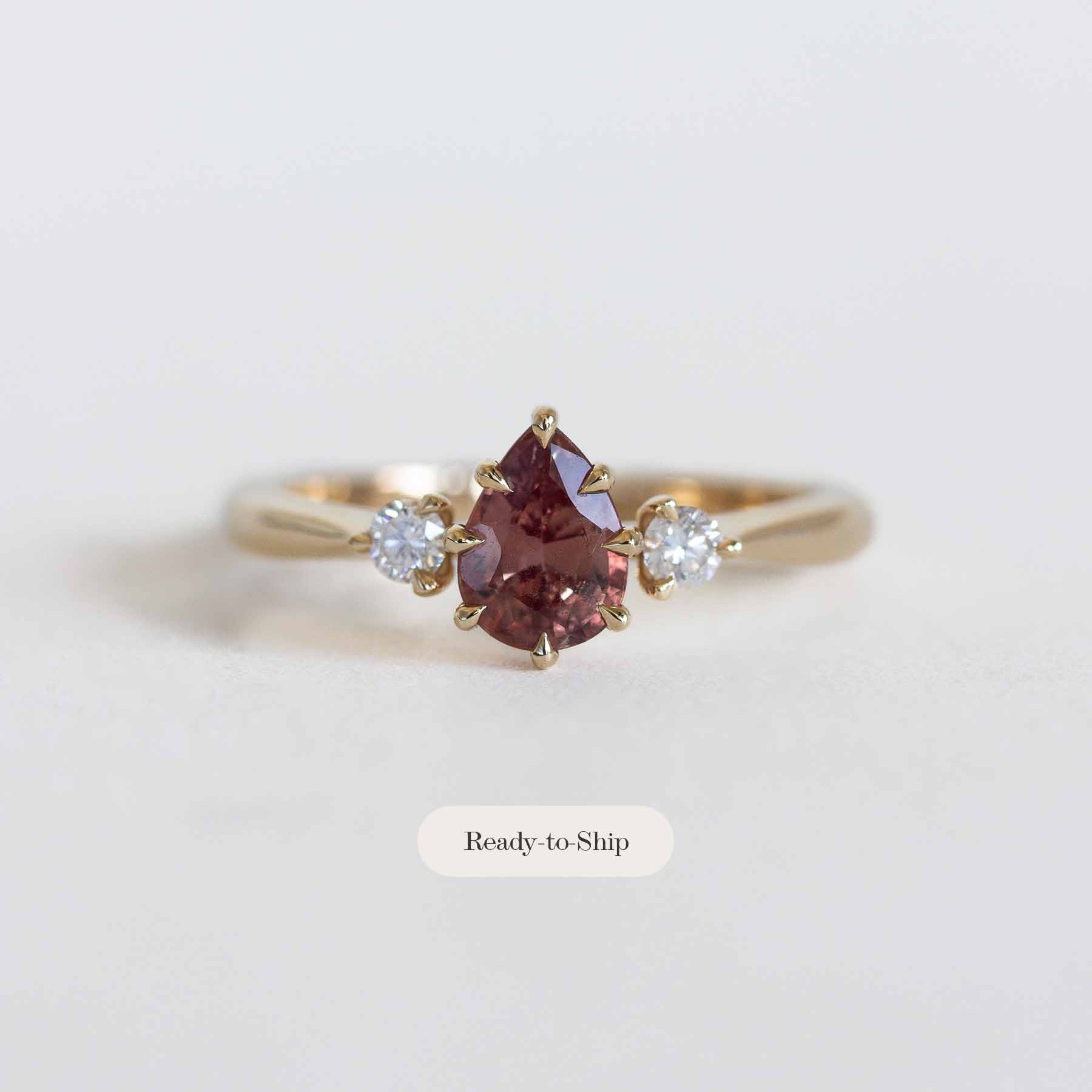 Gold ring with a berry sapphire and two smaller diamonds on a light gray background.