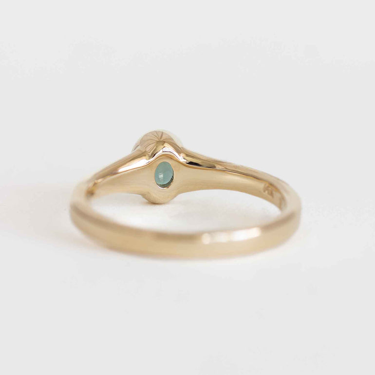 Gold ring with a green gemstone on a light gray background