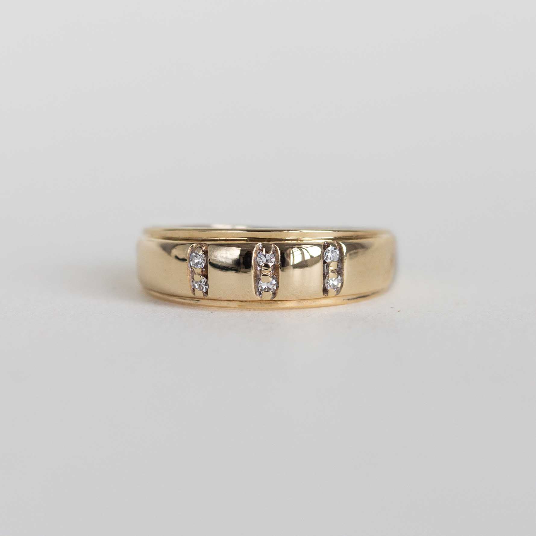 A yellow gold band ring featuring three vertical channels of small clear stones, photographed on a plain light gray background.