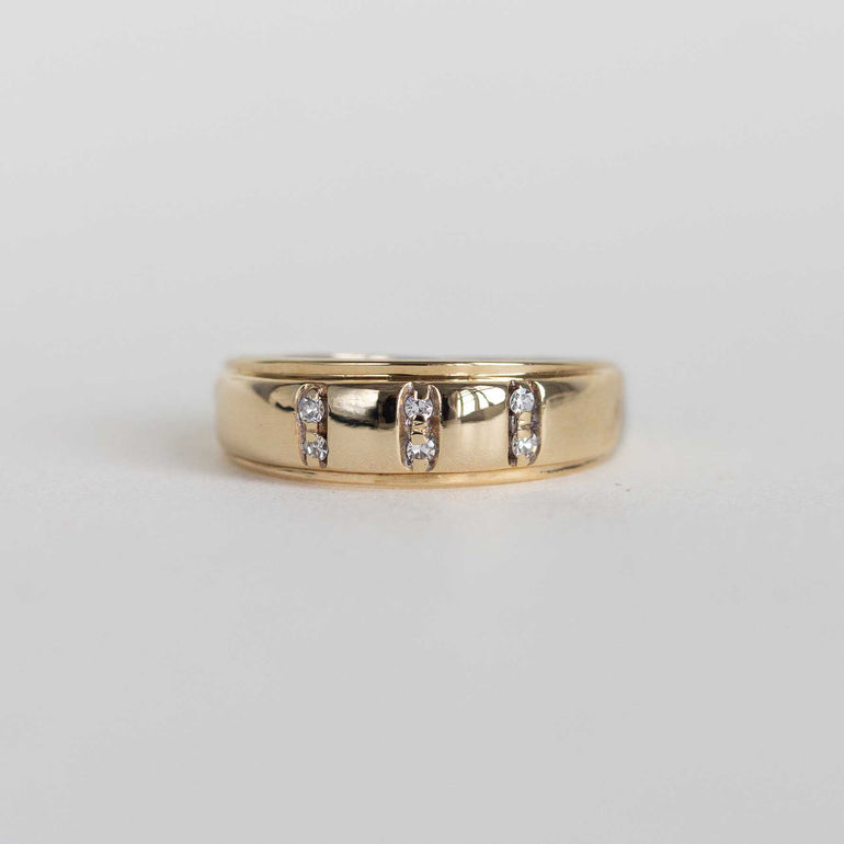 A yellow gold band ring featuring three vertical channels of small clear stones, photographed on a plain light gray background.