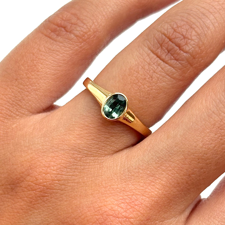 Gold ring with a green gemstone on a person's finger against a white background