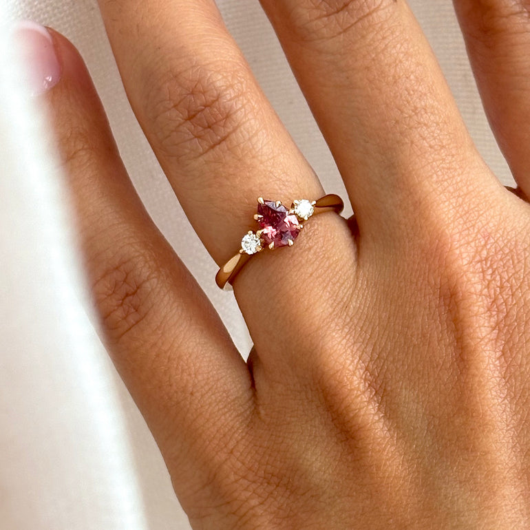 Close-up of a hand wearing a ring with a pink gemstone on a neutral background