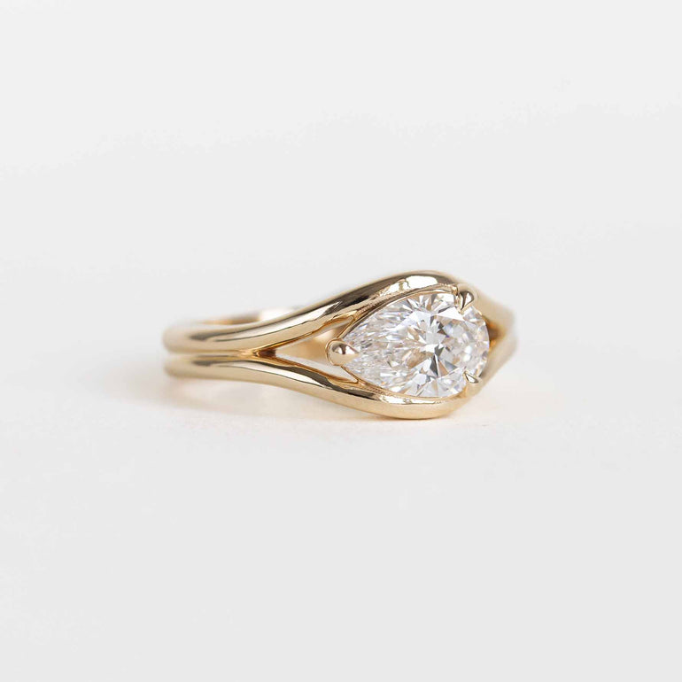 A yellow gold ring featuring a pear-cut lab diamond in a split bypass setting shown on a clean white background.
