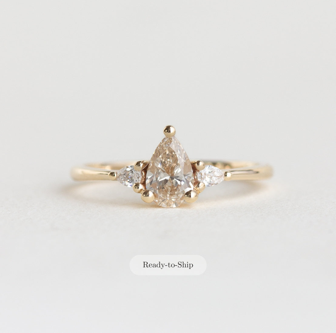 Gold ring with a pear-shaped diamond on a light gray background