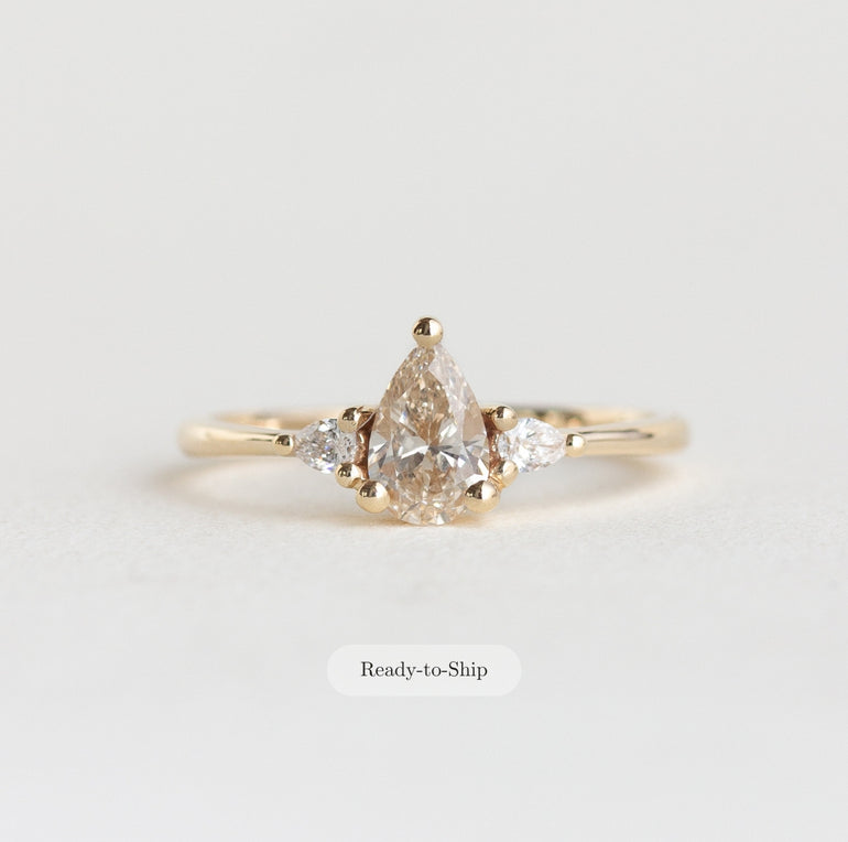 Gold ring with a pear-shaped diamond on a light gray background