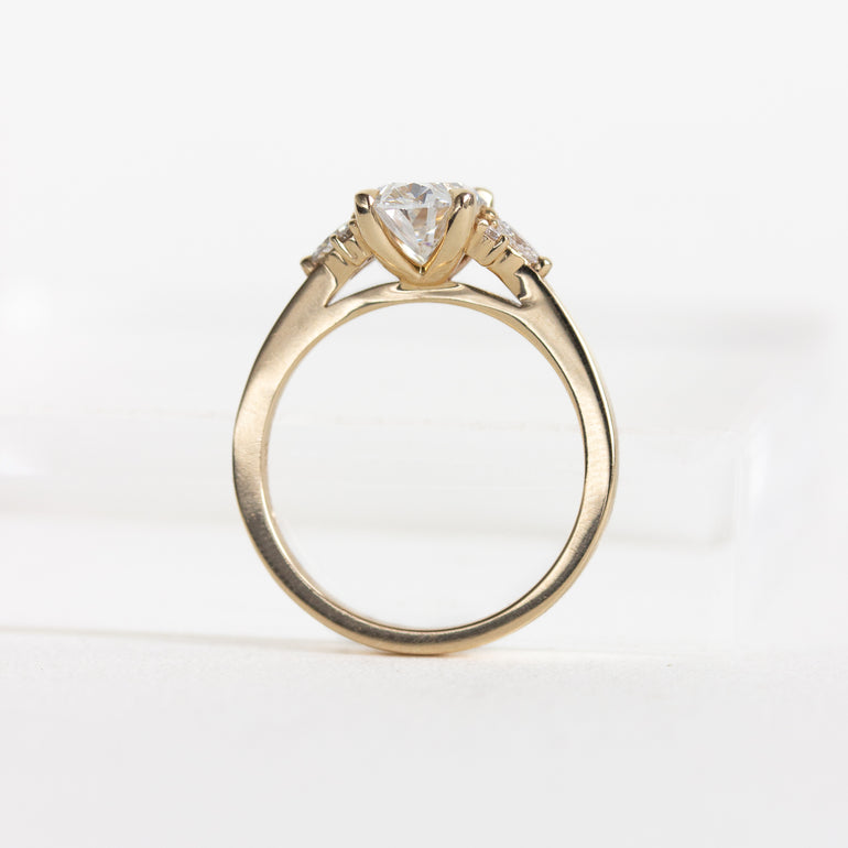 A yellow gold solitaire engagement ring with an oval diamond and small side stones, shown on a plain white background.