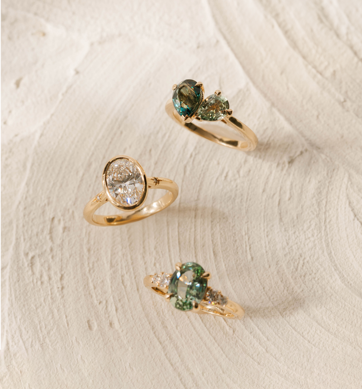 Three gold rings with gemstones on a textured beige surface