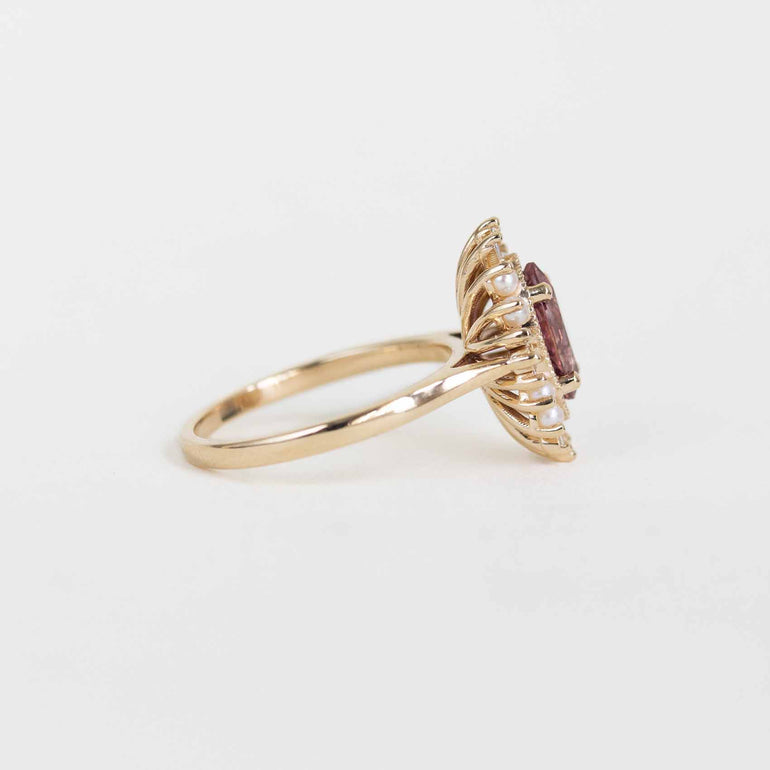 A gold ring with a floral cluster setting featuring a central oval purple gemstone and small clear accent stones, shown on a plain light gray background.