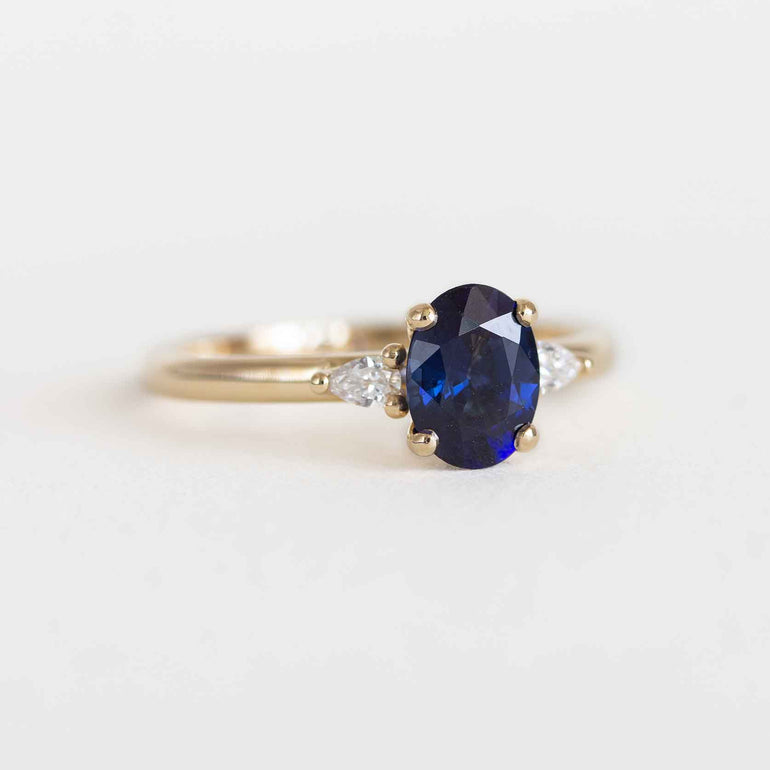 Blue sapphire engagement ring with pear diamond side stones and a yellow gold band