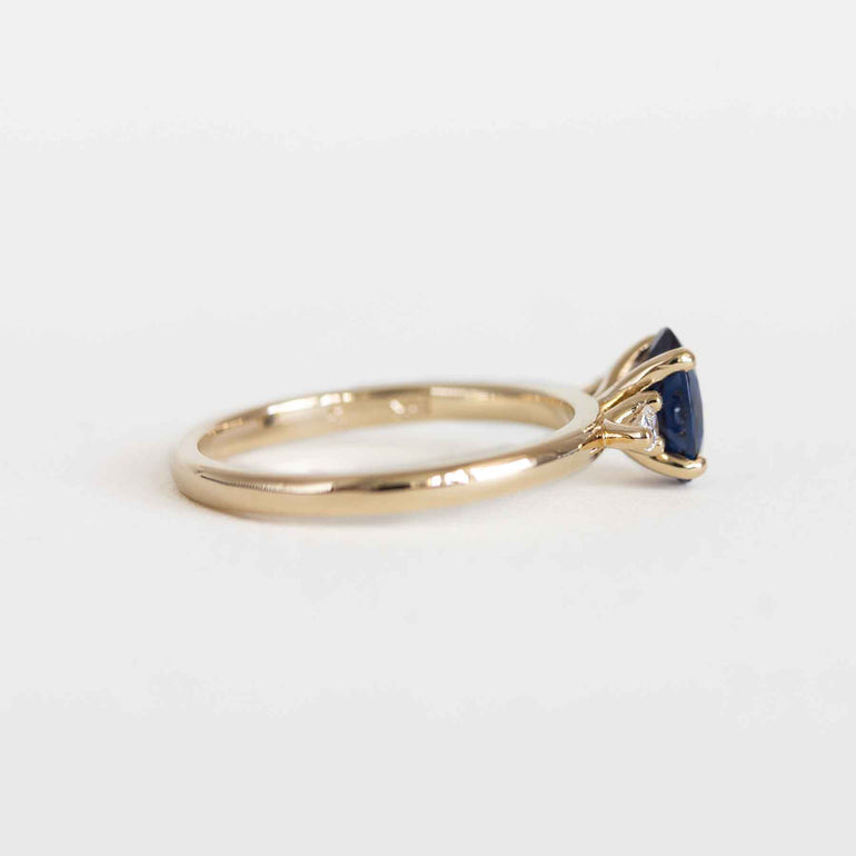 Blue sapphire engagement ring with pear diamond side stones and a yellow gold band