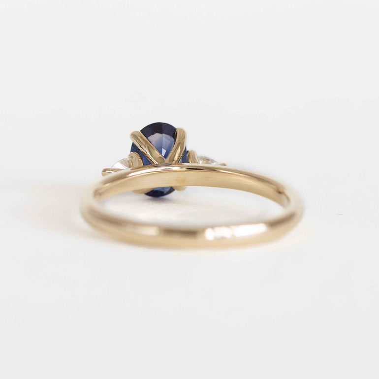 Blue sapphire engagement ring with pear diamond side stones and a yellow gold band