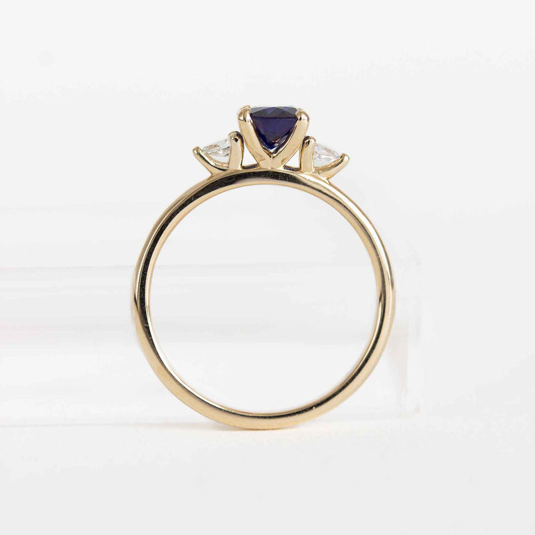 Blue sapphire engagement ring with pear diamond side stones and a yellow gold band