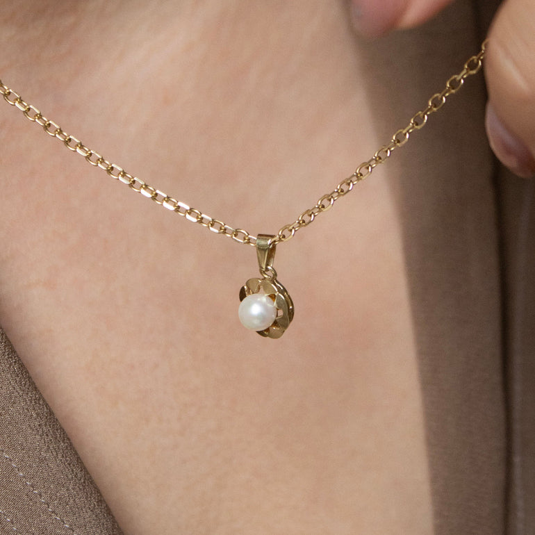 Gold necklace with a pearl pendant worn by a person