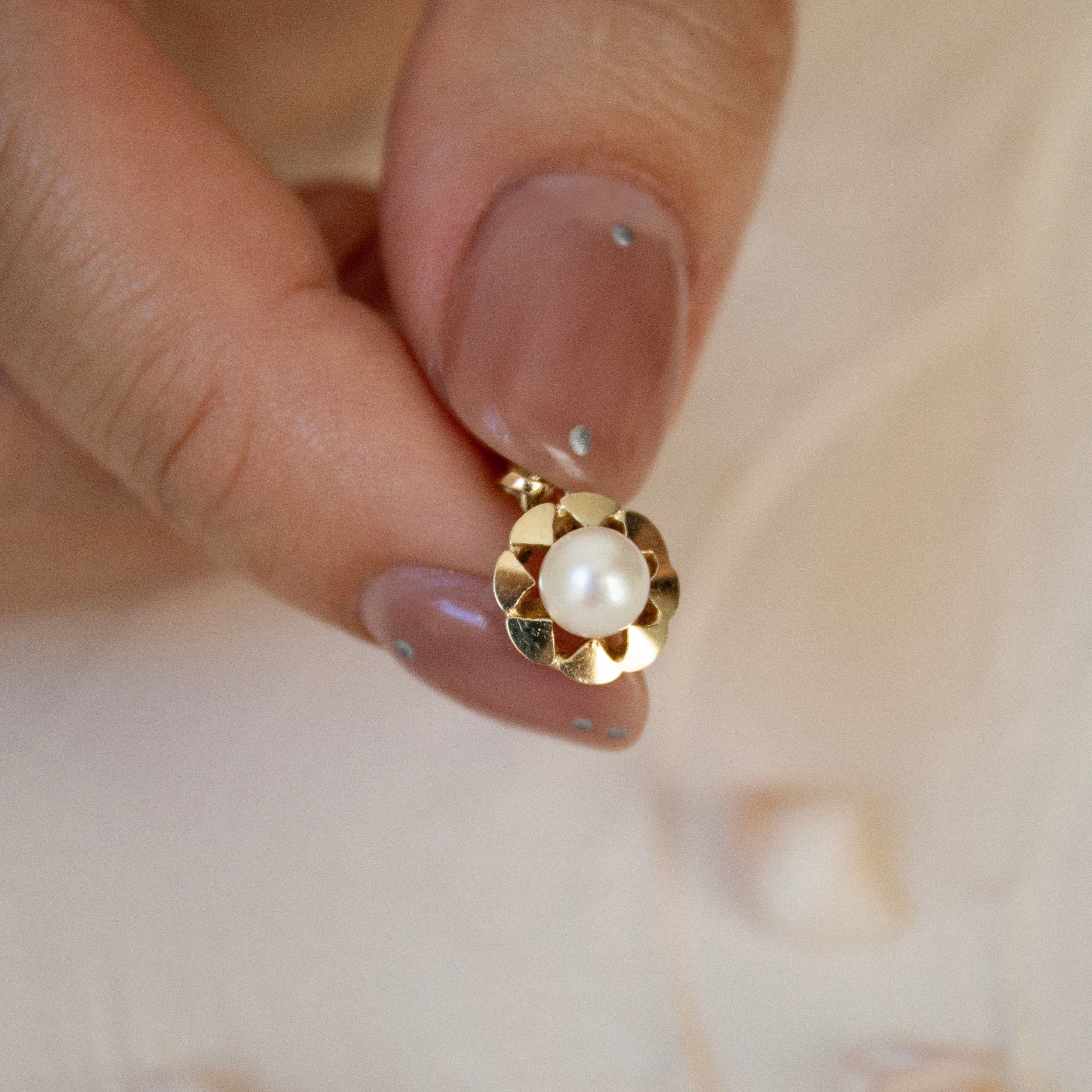 Gold earring with a pearl on a hand against a shell background