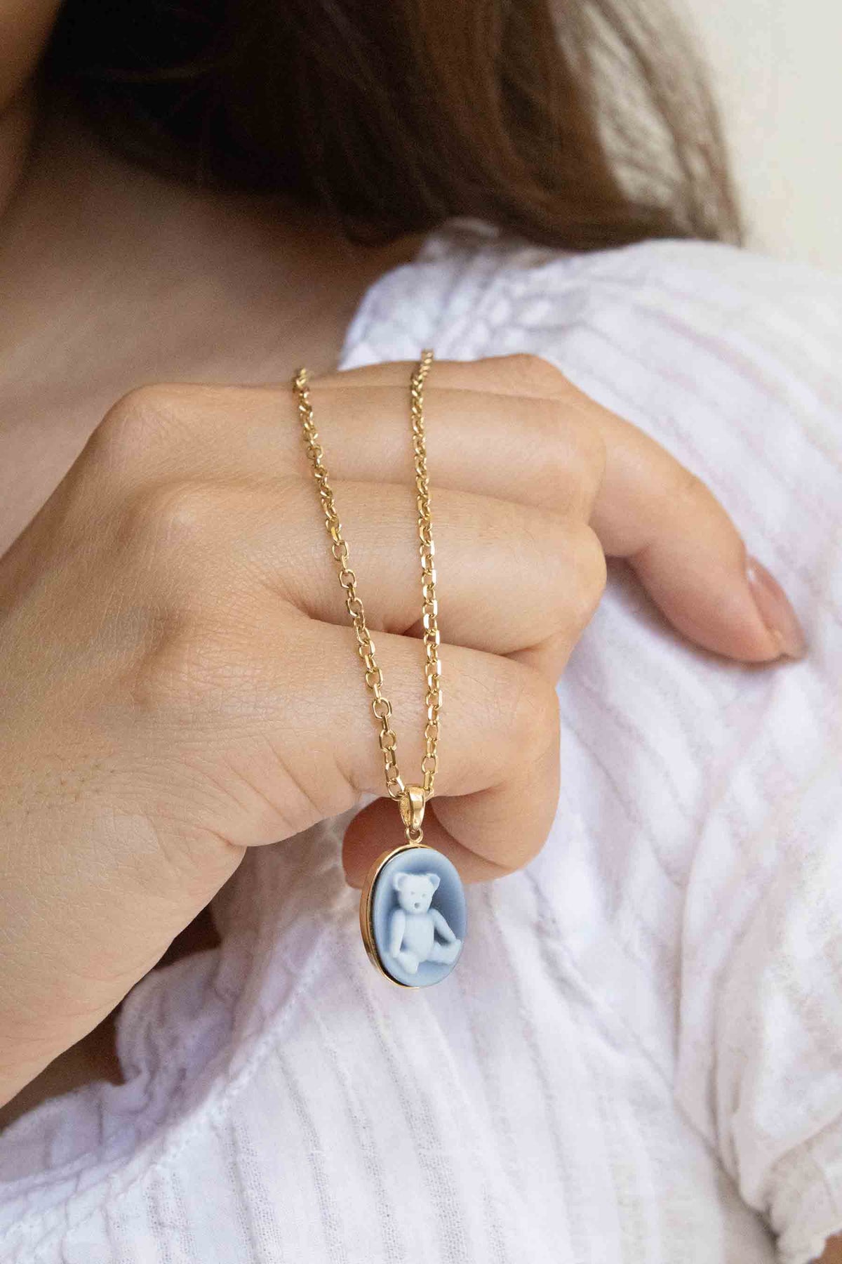 A teddy bear pendant hanging on a chain held by a hand