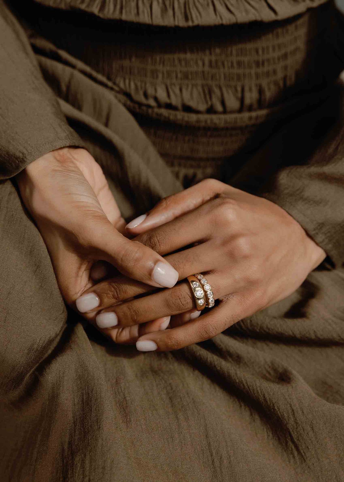 A close up of a woman's hands wearing two rings with a green outfit background