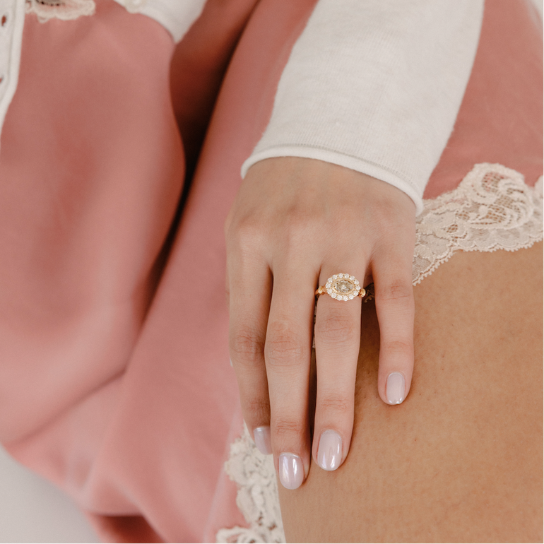 Close-up of a hand wearing a gold ring with a white lace glove and pink dress.