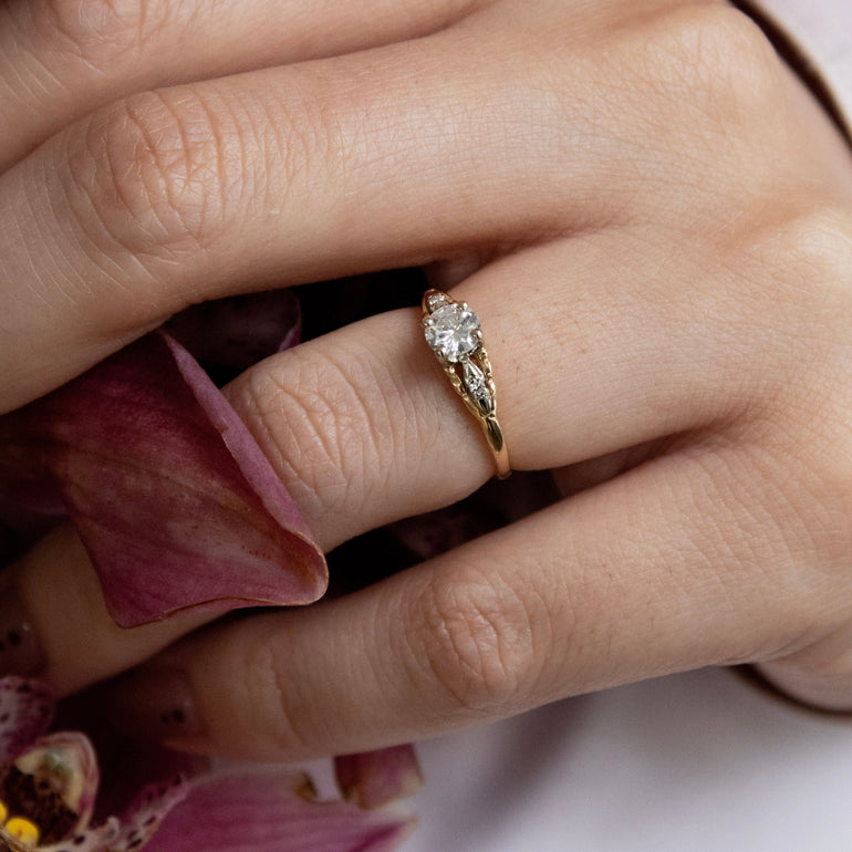 Close-up of a hand wearing a gold ring with a diamond, holding pink flowers.