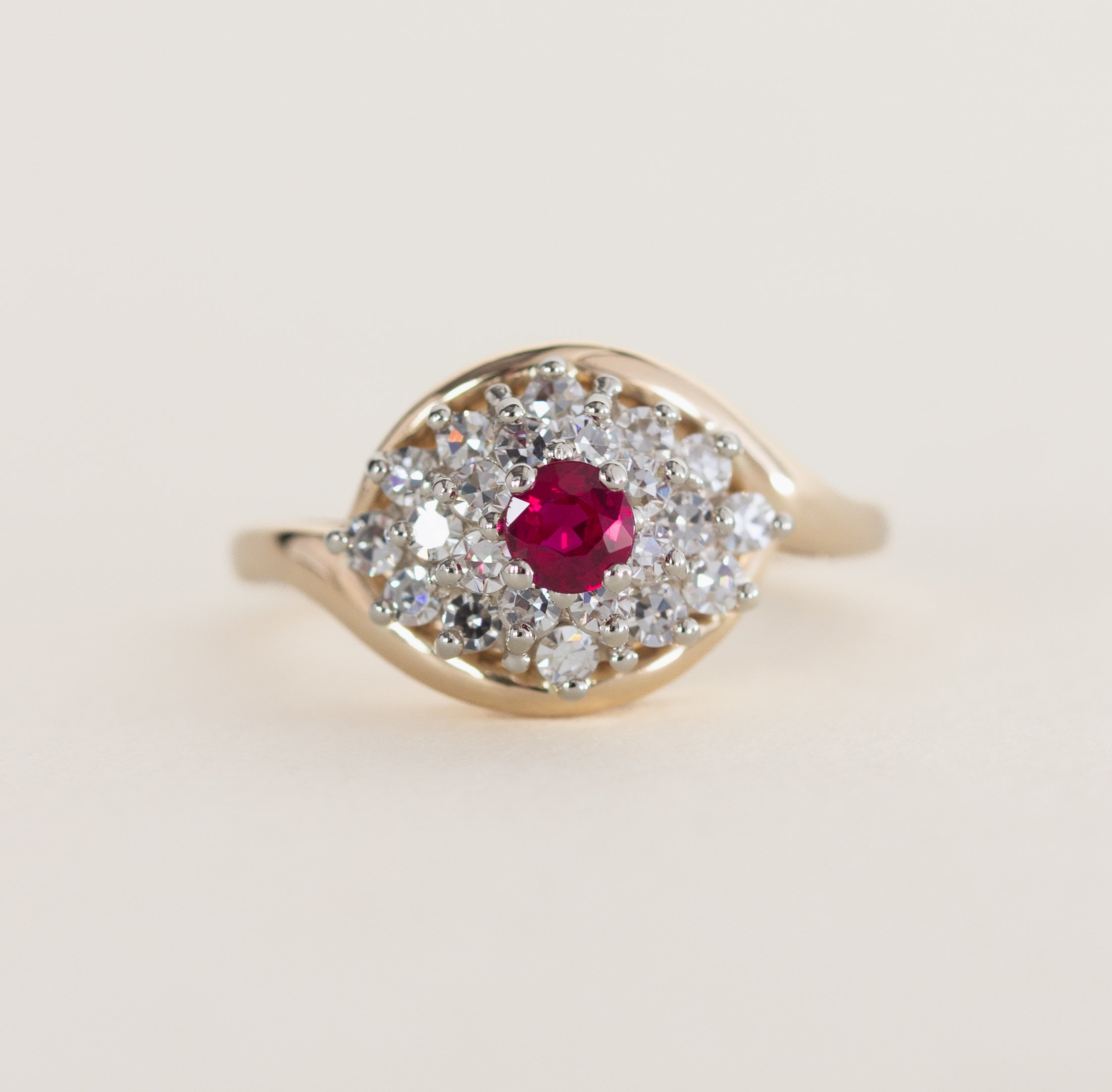 Gold ring with a red gemstone and diamond accents on a light beige background