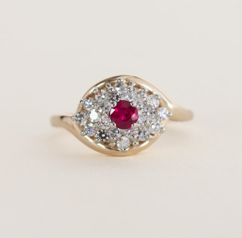 Gold ring with a red gemstone and diamond accents on a light beige background